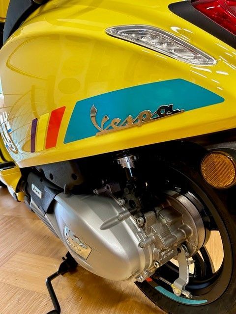Gelber Vespa-Roller mit blauem und goldenem Logodetail; silberner Motor.