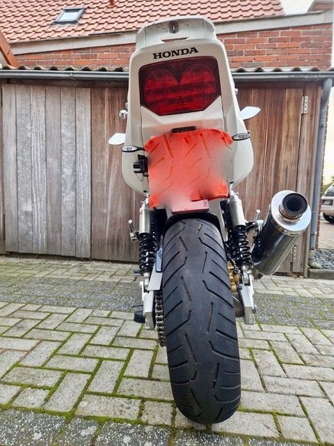 Rückansicht eines weißen Honda-Motorrads mit schwarzem Reifen, Rücklicht und Auspuff, auf einem Ziegelstein geparkt.