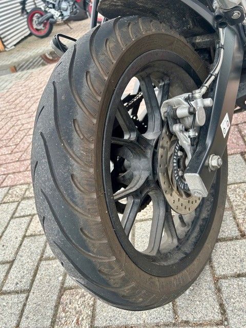 Nahaufnahme eines Motorradhinterrads und einer Scheibenbremse auf einer asphaltierten Oberfläche