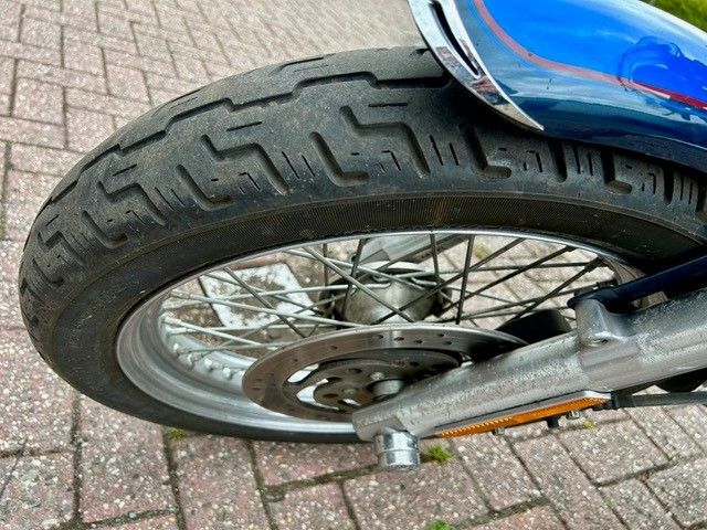 Nahaufnahme eines Motorradreifens und -rads mit blauem Kotflügel. Der Reifen hat ein abgenutztes Profil.