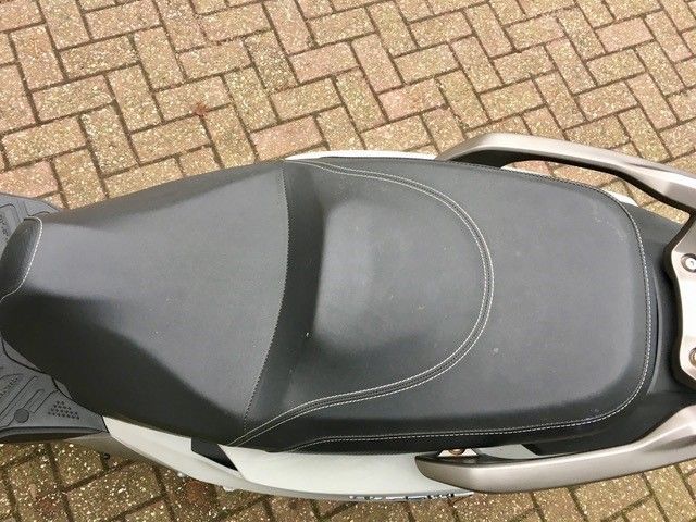 Ein schwarz-weißer Motorroller ist auf einem gepflasterten Gehweg geparkt.