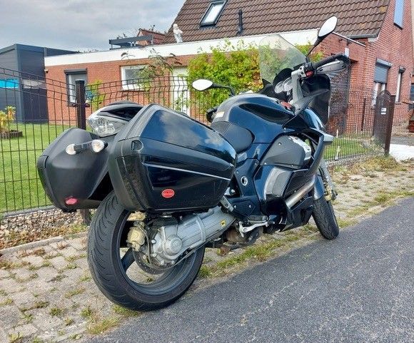 Schwarzes Motorrad mit Satteltaschen, geparkt auf einem Bürgersteig vor einem Haus.