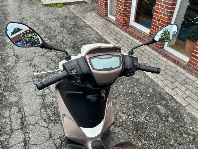 Schwarzer und beiger Roller parkt auf einer rissigen Straße, Ansicht von oben.