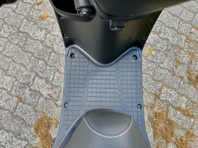 Ein schwarzer Motorroller ist auf einem gepflasterten Gehweg geparkt.
