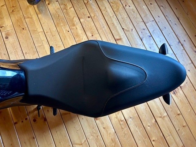 Schwarzer Motorradsitz auf einem Holzboden, von oben betrachtet.