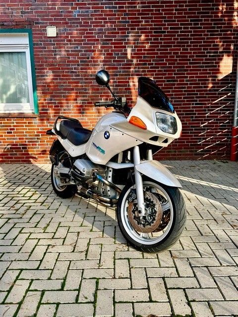 Auf einer gepflasterten Auffahrt vor einem Backsteingebäude ist ein Motorrad geparkt.