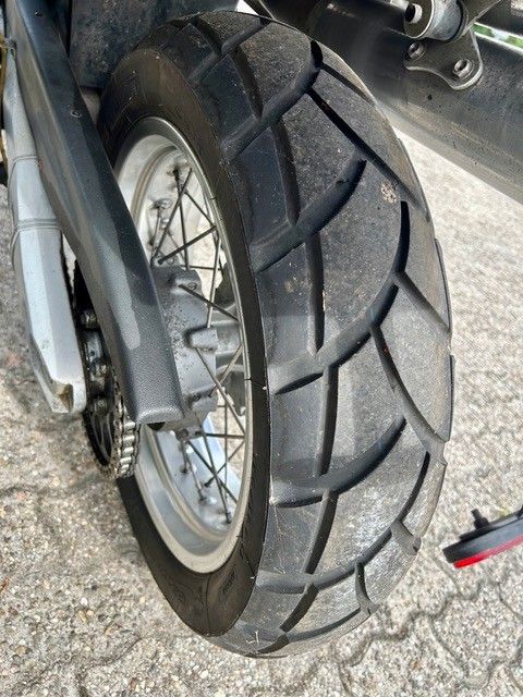 Nahaufnahme eines Motorradhinterreifens mit tiefem Profil auf einer asphaltierten Fahrbahn.