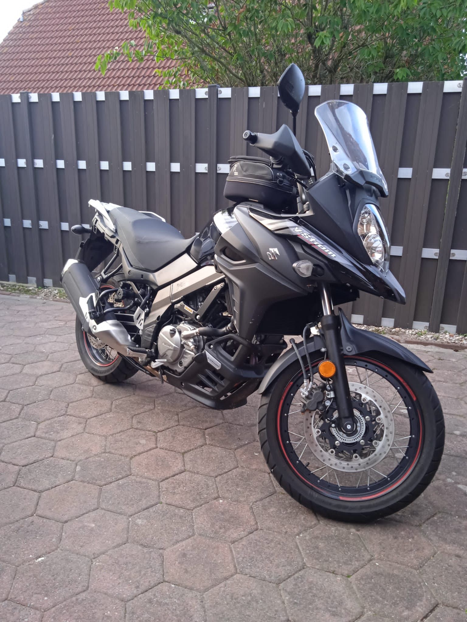 Vor einem Holzzaun parkt ein schwarzes Motorrad.