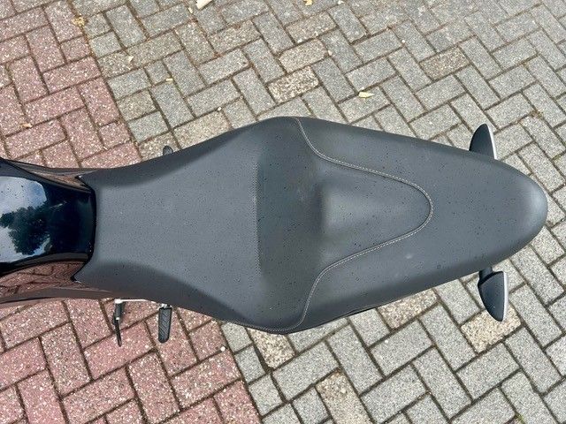 Schwarzer Motorradsitz auf einem geparkten Motorrad auf einem mit Ziegeln gepflasterten Untergrund.