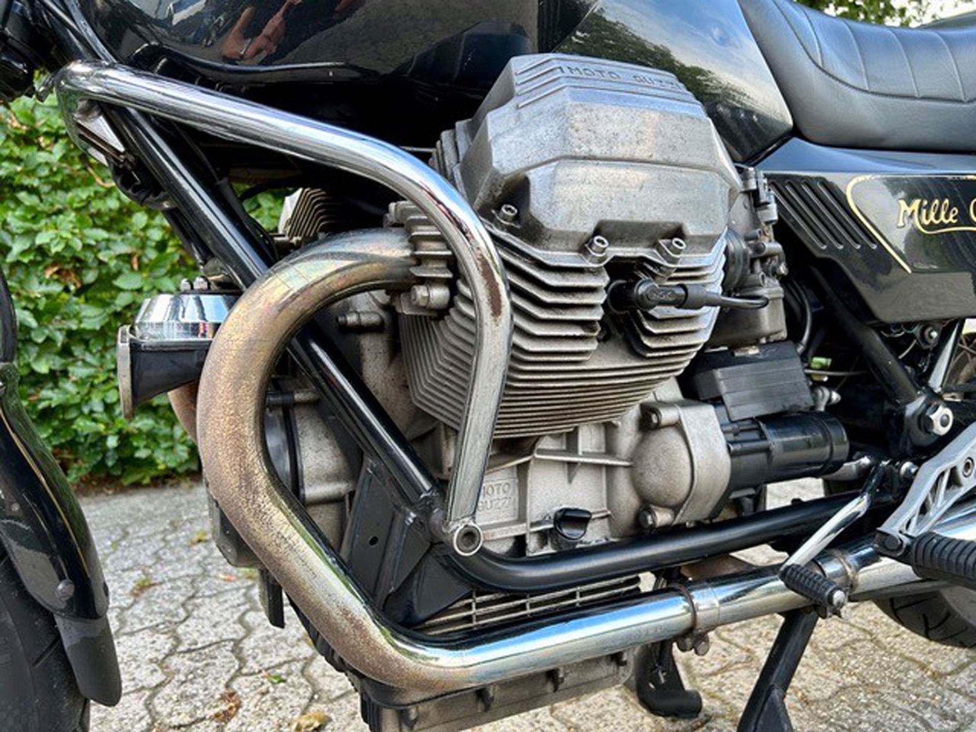 Seitenansicht eines schwarzen Moto Guzzi Mille GT-Motorradmotors mit verchromten Sturzbügeln. Grauer Motor, schwarzer Rahmen und poliertes Chrom.