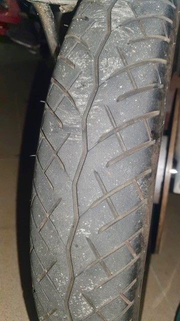 Nahaufnahme eines Motorradreifens mit abgefahrenem Profil, das diagonale und longitudinale Rillen aufweist.