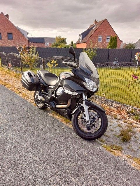Schwarzes Tourenmotorrad auf dem Bürgersteig geparkt, im Hintergrund ein bewölkter Himmel und Häuser.