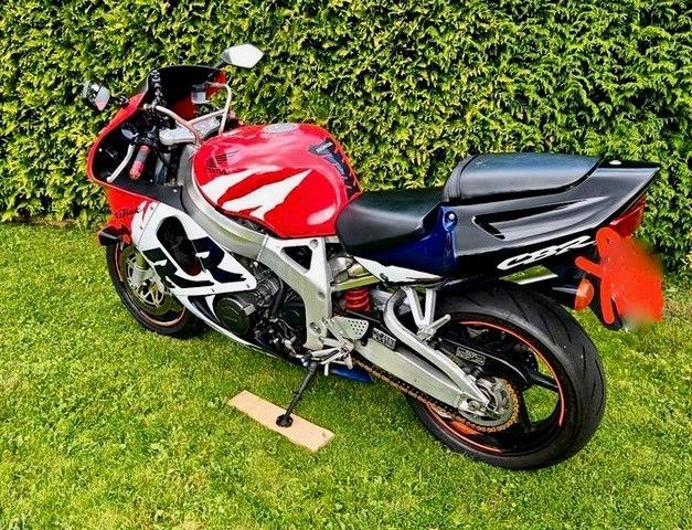 Rot-weiß-blaues Honda CBR-Motorrad auf grünem Gras geparkt.