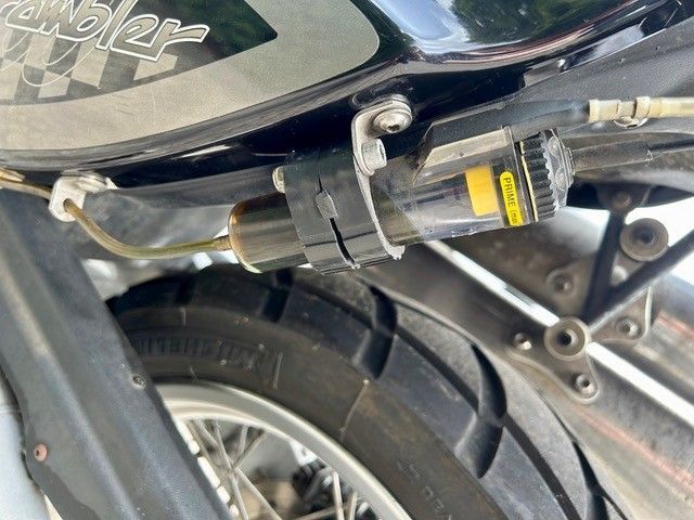 Nahaufnahme eines Motorradhinterrads, der Kette und des Kabels unter dem Sitz, mit einem schwarz-silbernen Rahmen.
