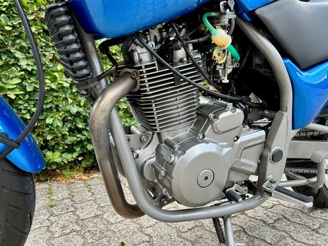 Blauer Motorradmotor mit Auspuffrohr, grauem Rahmen und Vergasern im Freien.