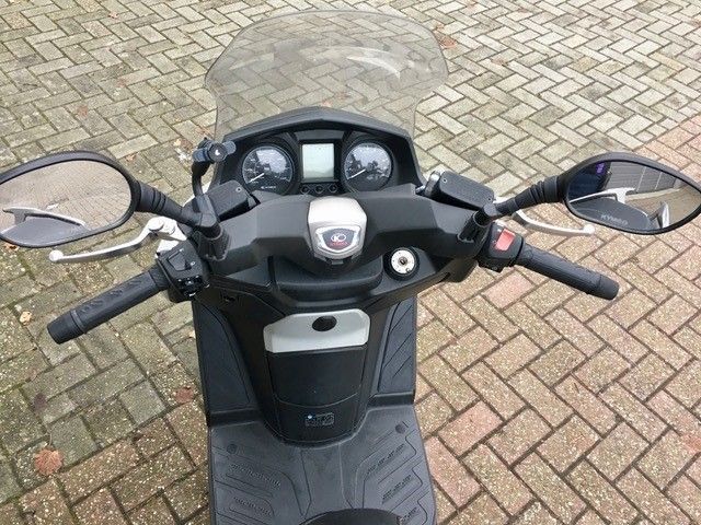 Die Vorderseite eines Motorrollers ist auf einem Ziegelsteinpflaster geparkt.