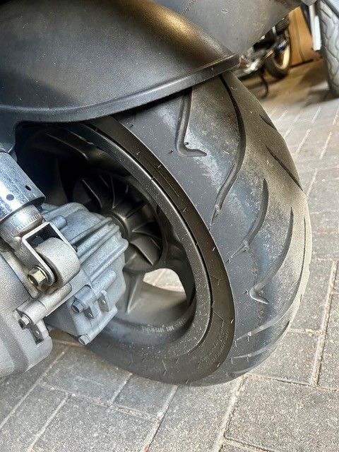 Nahaufnahme eines Rollerhinterrads und -reifens auf einer asphaltierten Oberfläche
