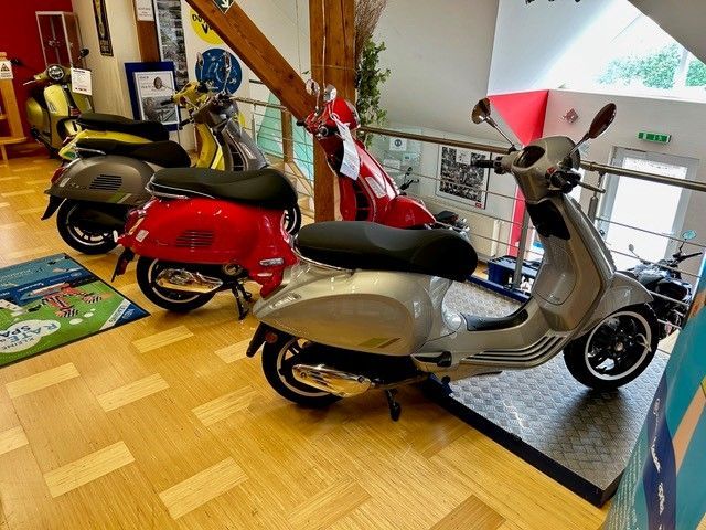 Mehrere Vespa-Roller in verschiedenen Farben sind im Innenbereich ausgestellt.