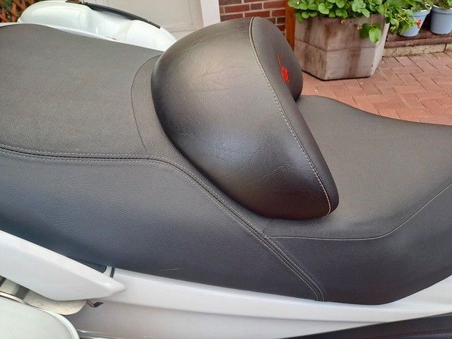 Schwarzer Motorradsitz mit gepolsterter Rückenlehne, im Freien. Der Sitz befindet sich auf einem weißen Roller.