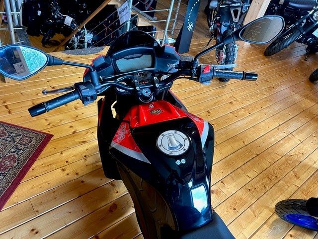 Ein rot-schwarzes Motorrad, von oben betrachtet, steht auf einem Holzboden in einer Garage.