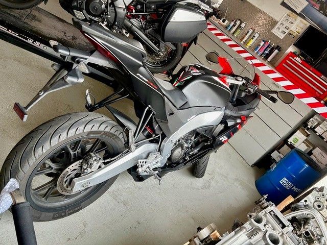 Schwarz-silbernes Motorrad, das in einer Garage geparkt ist; Ansicht von der Seite, Hinterrad und Motor sind sichtbar.