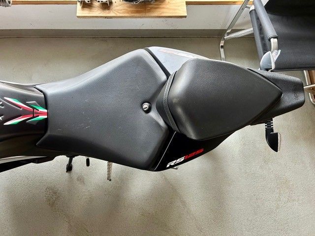 Schwarzer Motorradsitz und Heckverkleidung im Innenbereich, mit einem kleinen weiß-roten Logo.