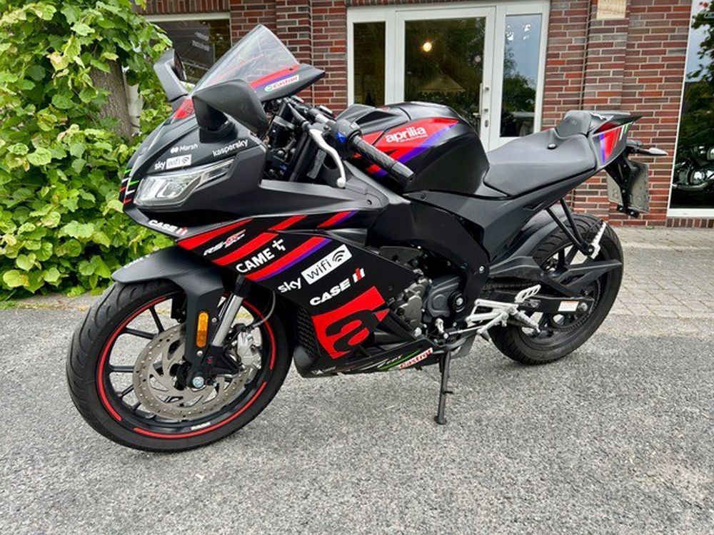 Ein schwarz-rotes Sportmotorrad parkt auf einer Einfahrt vor einem Backsteinhaus.