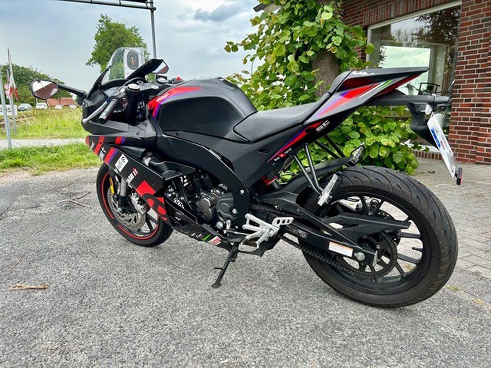 Ein schwarz-rotes Sportmotorrad parkt im Freien neben einem Backsteingebäude und einer efeubewachsenen Mauer.