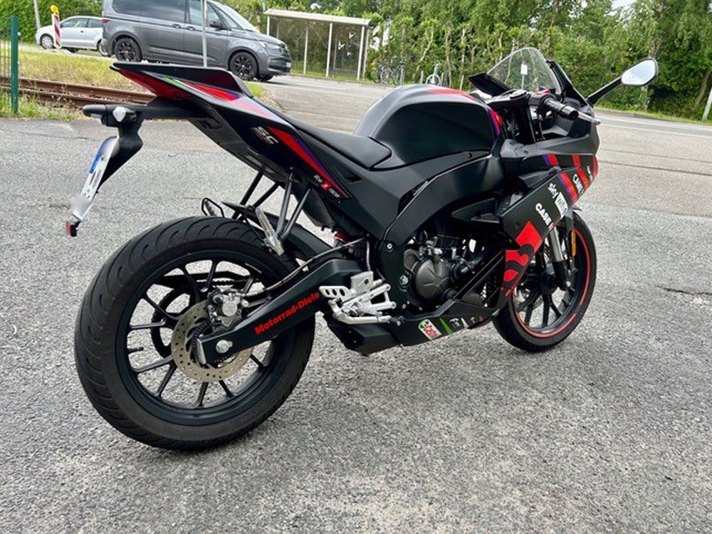 Ein schwarzes und rotes Sportmotorrad parkt am Straßenrand, im Hintergrund ist ein Auto zu sehen.