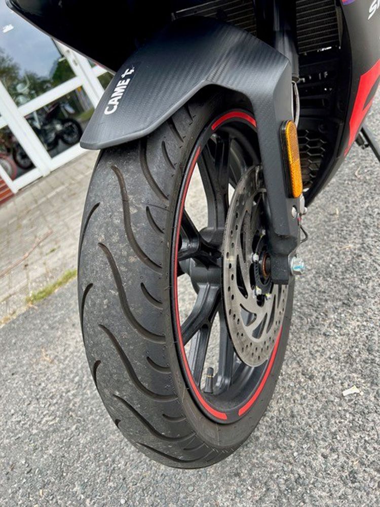 Nahaufnahme eines Motorradvorderrads mit schwarzem Reifen, roten Felgenakzenten und Scheibenbremse auf Asphalt