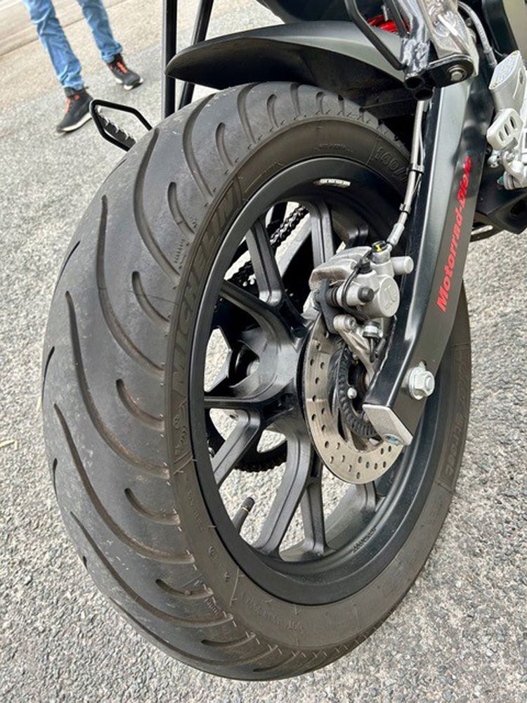 Nahaufnahme des Hinterrads, des Reifens und der Scheibenbremse eines Motorrads auf Asphalt.