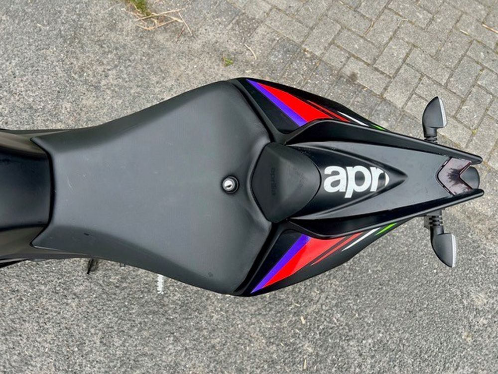 Draufsicht auf einen schwarzen Motorradsitz mit roten und blauen Akzenten auf einer gepflasterten Oberfläche