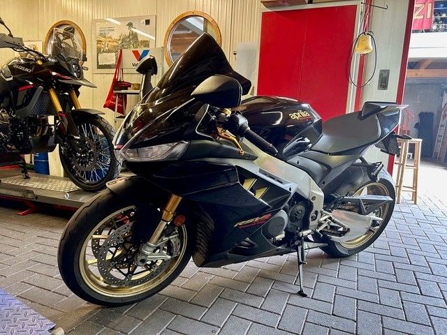 Ein schwarzes Sportmotorrad steht in einem Innenraum auf einem gefliesten Boden; im Hintergrund sind eine rote Tür und ein weiteres Motorrad zu sehen.