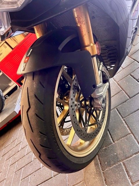 Nahaufnahme eines Motorradhinterrads mit Reifen auf einer gepflasterten Straße, mit sichtbarem roten Rücklicht.