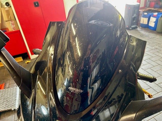 Schwarze Motorradfrontverkleidung in einer Werkstatt mit roten Schränken und Werkzeugen im Hintergrund