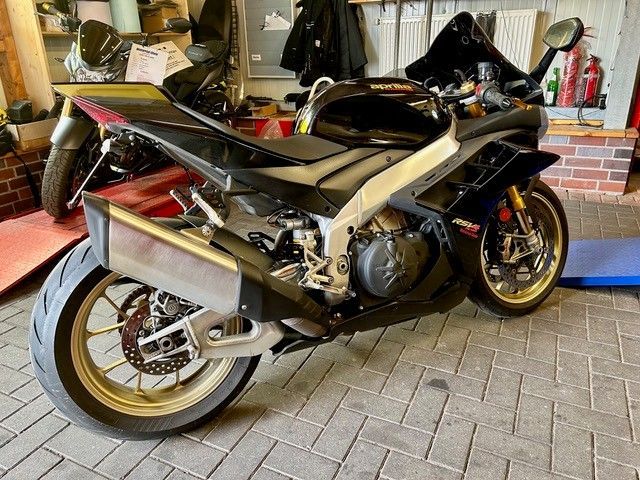 Ein schwarzes und silbernes Sportmotorrad parkt auf einer gepflasterten Auffahrt unter einem Carport.