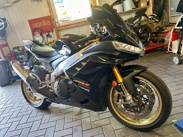 Schwarzes Sportmotorrad mit goldenen Felgen, das in einer Garage parkt.