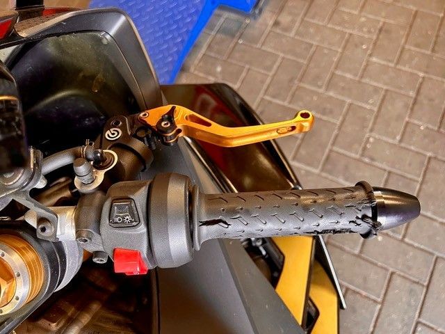 Motorradlenker und Bremshebel mit schwarzem Griff und rotem Schalter, geparkt auf einem Ziegelpflaster.