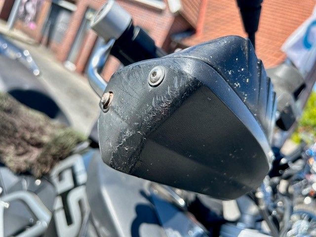 Eine Nahaufnahme des Lenkers eines Motorrads mit einem Backsteingebäude im Hintergrund.