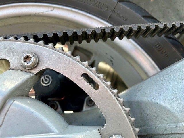 Nahaufnahme einer Fahrradkette mit Zahnradmechanismus, die Metallzähne und Riemenantrieb zeigt.