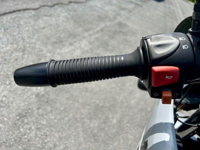 Motorradlenker mit schwarzem Griff und rotem Schalter auf grauem Straßenhintergrund