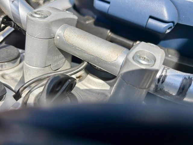 Nahaufnahme eines silbernen Metallscharniers oder einer Halterung mit Schrauben auf einer blauen Fahrzeugoberfläche