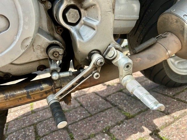 Nahaufnahme eines Motorradmotors mit Fußrasten und Auspuffrohr auf einer gepflasterten Auffahrt
