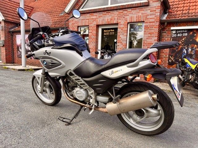 Ein silber-schwarzes Motorrad parkte auf einer Kopfsteinpflasterstraße vor einem Backsteingebäude.