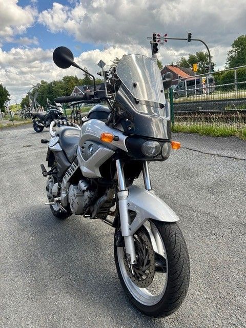 Ein silbernes Tourenmotorrad parkt auf einer Straße in der Nähe eines Kanals und von Häusern unter bewölktem Himmel.