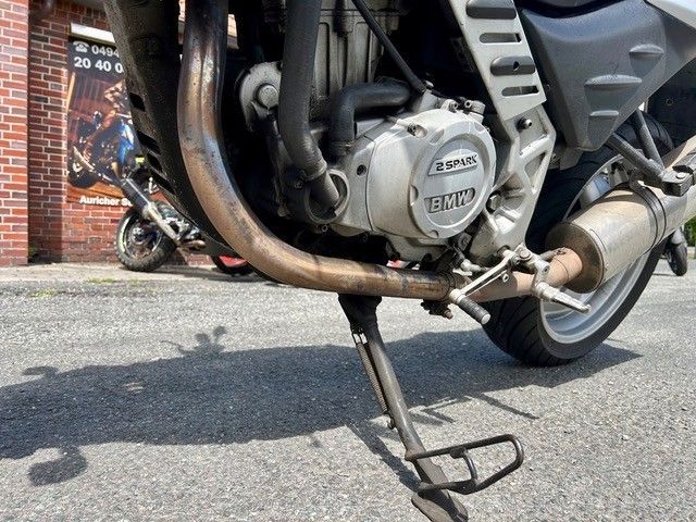 Nahaufnahme eines Motorradmotors und Seitenständers, die auf einer Straße geparkt sind.
