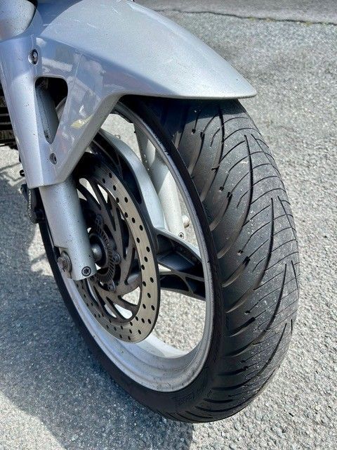 Vorderrad eines silbernen Rollers mit Scheibenbremse auf einer asphaltierten Straße