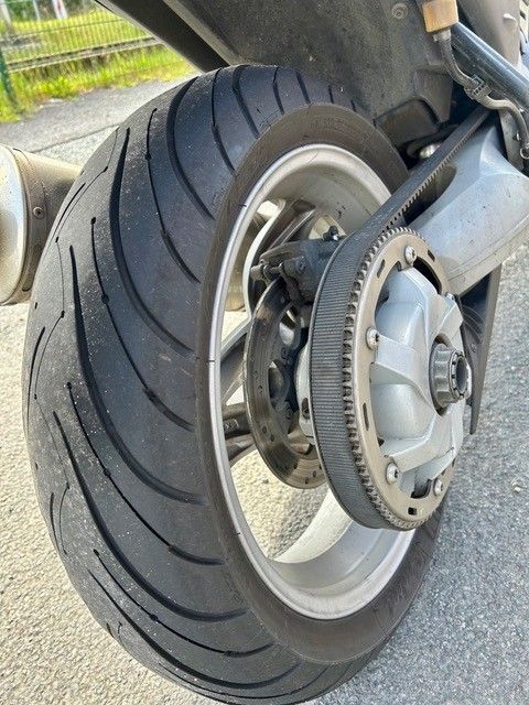 Nahaufnahme eines Motorradhinterrads mit Reifenprofil und Bremsscheibe, von der Seite betrachtet.