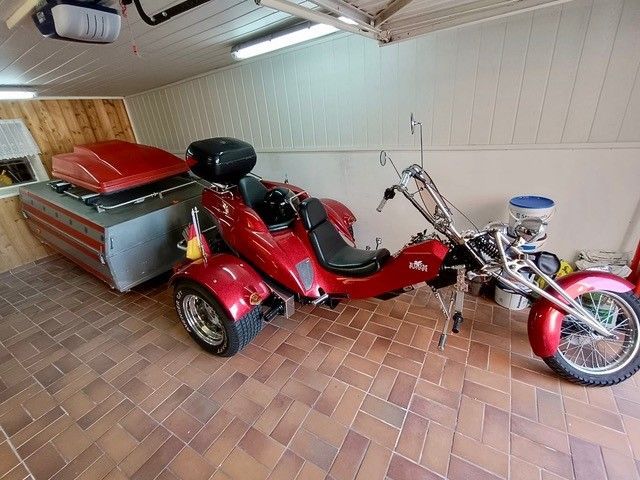 Ein rotes Dreirad steht in einer Garage neben einem Motorrad.