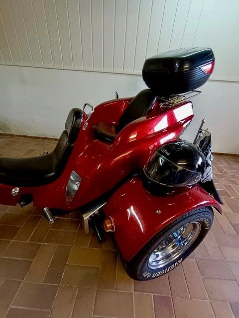 Ein rotes Motorrad mit drei Rädern ist auf einem gefliesten Boden geparkt.